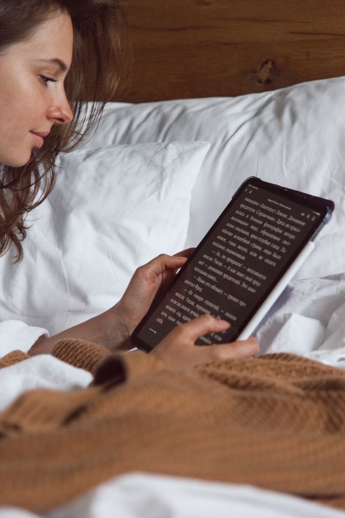 A woman reading on her tablet while lying in bed, creating a cozy and relaxed atmosphere.